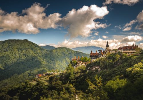 An aerial shot of a small village on the hill surrounded by forested mountains